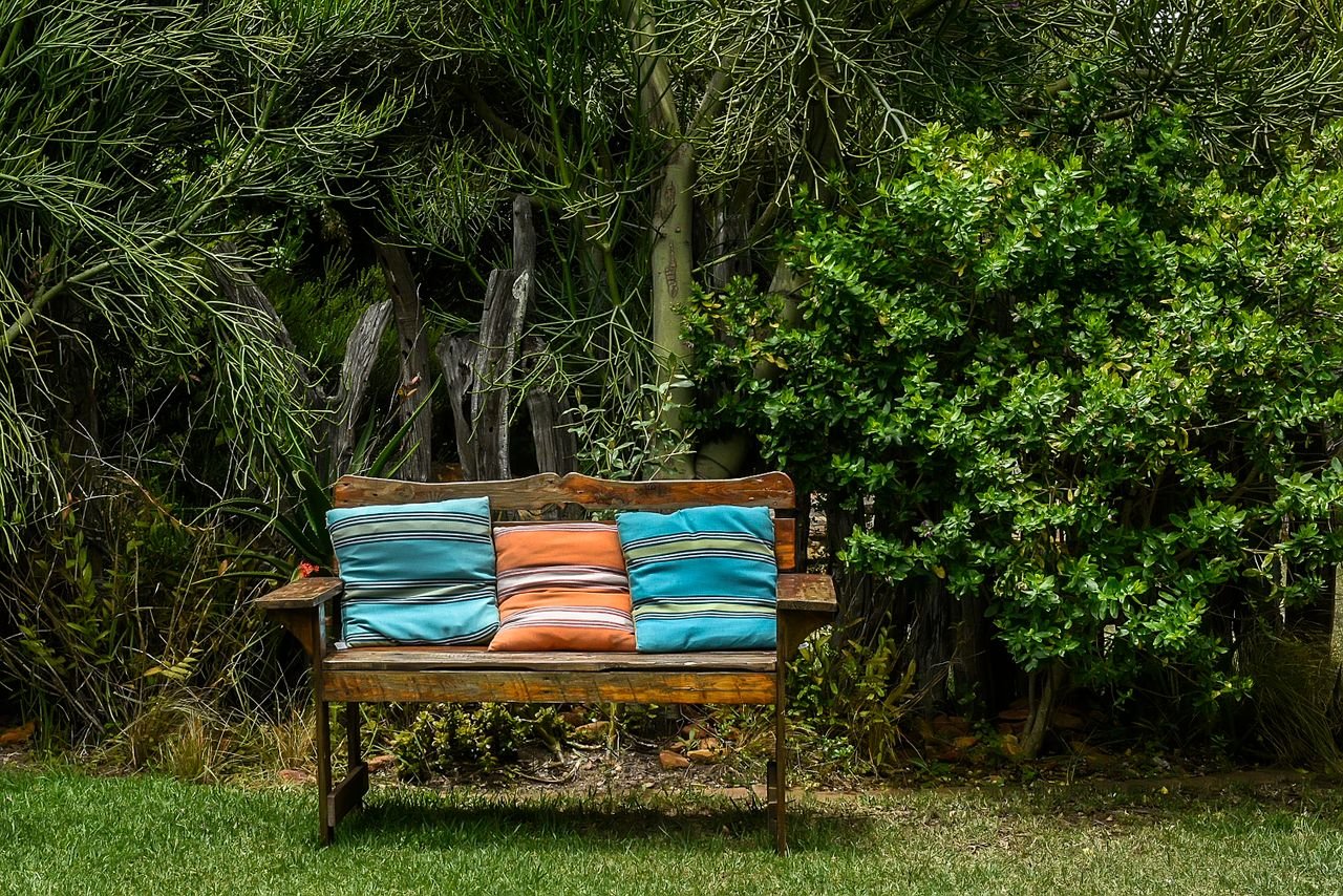 A wooden bench with bright cushions sits in a lush green garden, creating a tranquil outdoor space.